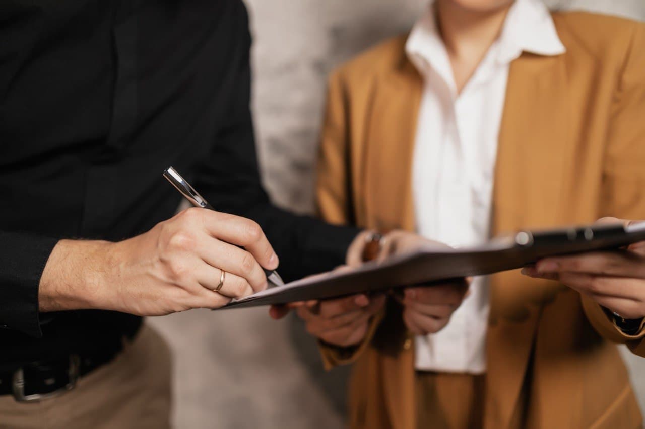 Close-up of a tenant signing a lease document held on a clipboard by another person